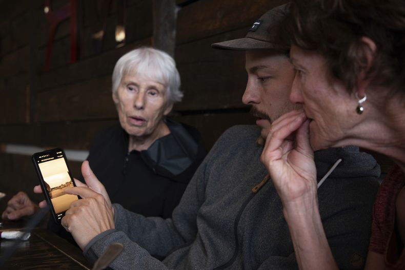 Los evacuados del incendio forestal de Jasper, de izquierda a derecha, Gina Jabes, Jeremie Rodger, y Loni Klettl, miran fotos de la devastación en Jasper, tratando de reconocer las zonas que conocían tan bien, desde un restaurante en Hinton, Alberta, el jueves 25 de julio de 2024. (Amber Bracken/The Canadian Press vía AP)