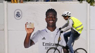 Un ciclista pasa frente a un afiche de Vinicius Junior, el delantero brasileño del Real Madrid, frente al estadio Santiago Bernábeu, el lunes 22 de mayo de 2023 en Madrid. (AP Foto/Paul White)