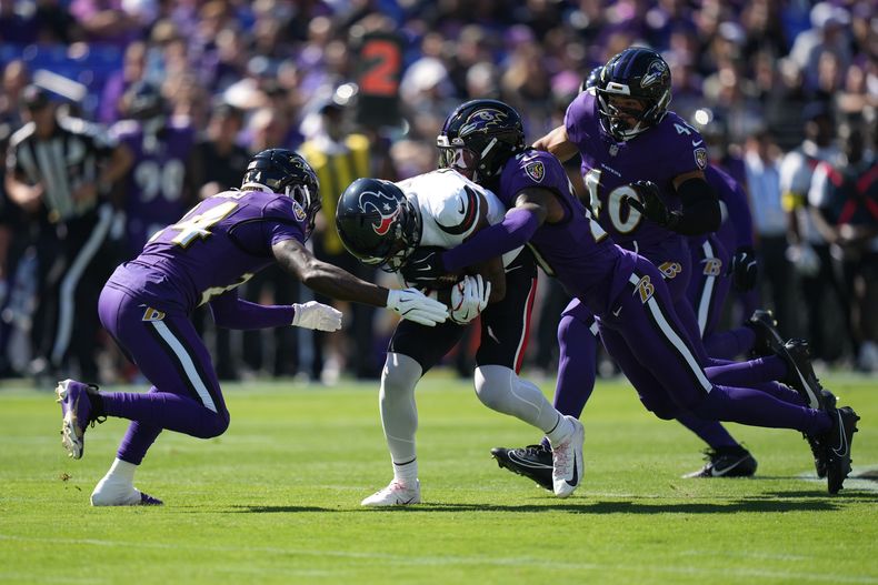Nico Collins, centro, wide receiver de los Texans de Houston, es derribado por el safety Malaki Starks, izquierda, y el cornerback T.J. Tampa (27). mientras el linebacker Teddye Buchanan (4), de los Ravens de Baltimore, observa, durante la primera mitad del partido de la NFL del domingo 5 de octubre de 2025, en Baltimore. (AP Foto/Stephanie Scarbrough)