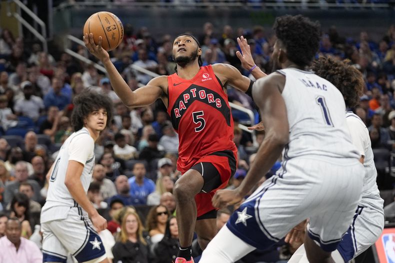 Immanuel Quickley (5), de los Raptors de Toronto, se cuela entre Anthony Black, izquierda, y Jonathan Isaac (1), del Magic de Orlando, para tomar buscar encestar una canasta durante la segunda mitad del juego de baloncesto de la NBA, el domingo 2 de marzo de 2025, en Orlando, Florida. (AP Foto/John Raoux)
