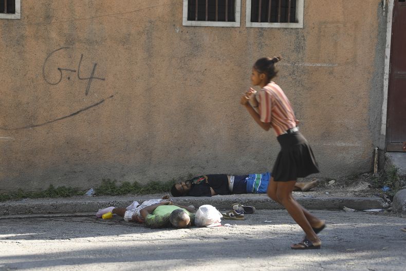 Una mujer pasa junto a los cuerpos de dos hombres asesinados por agresores desconocidos, el domingo 3 de marzo de 2024, en Puerto Príncipe, Haití. (AP Foto/Odelyn Joseph)