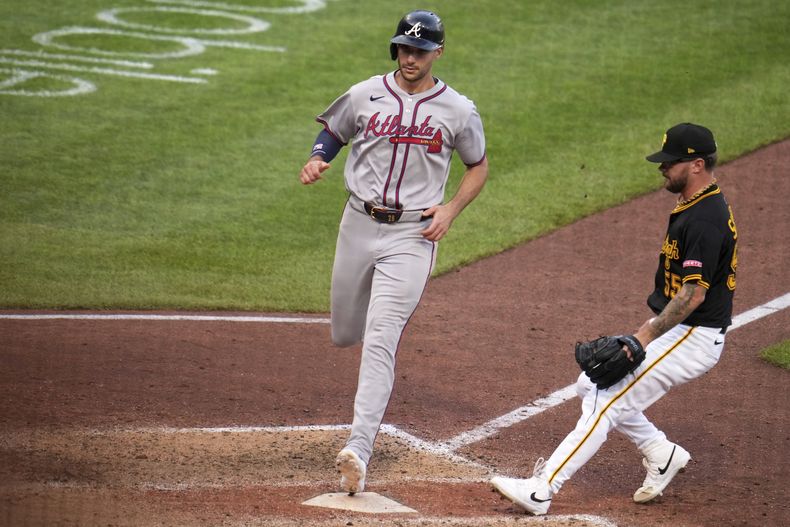 Matt Olson, de los Bravos de Atlanta, a la izquierda, anota desde la tercera base en un lanzamiento descontrolado del lanzador de los Piratas de Pittsburgh, Chase Shugart, a la derecha, durante la undécima entrada de un juego de béisbol en Pittsburgh, el sábado 10 de mayo de 2025. (AP Foto/Gene J. Puskar)