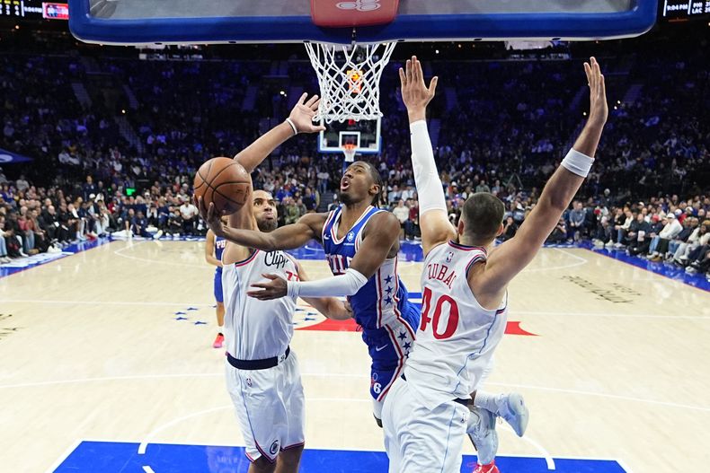 Tyrese Maxey, centro, de los 76ers de Filadelfia, se alza para encestar entre Nicolas Batum, izquierda, e Ivica Zubac, derecha, de los Clippers de Los Ángeles, durante la segunda mitad del juego de baloncesto de la NBA, el lunes 17 de noviembre de 2025, en Filadelfia. (AP Foto/Matt Rourke)