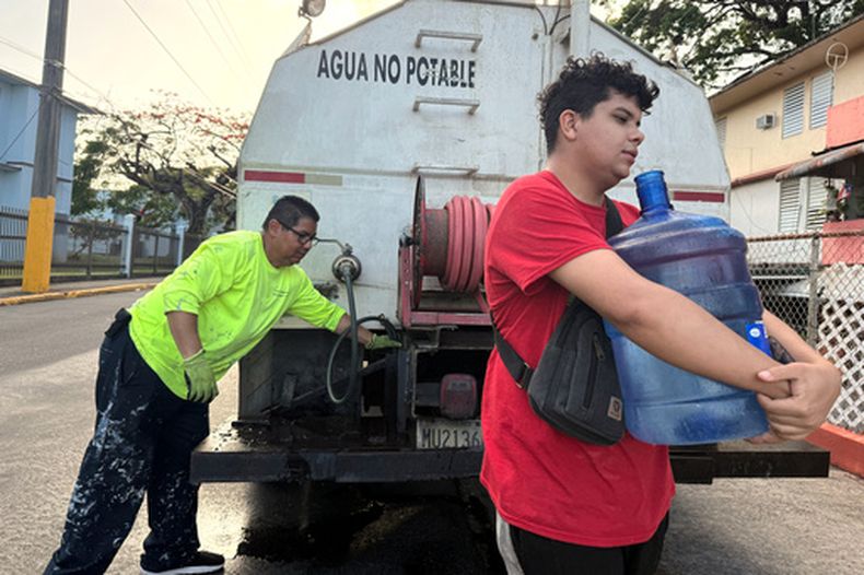 ARCHIVO - Bryan Pérez carga un bidón de cinco galones de agua hacia su apartamento en el complejo de vivienda pública Villa Kennedy, en San Juan, Puerto Rico, el 10 de junio de 2026. (AP Foto/Dánica Coto, Archivo)