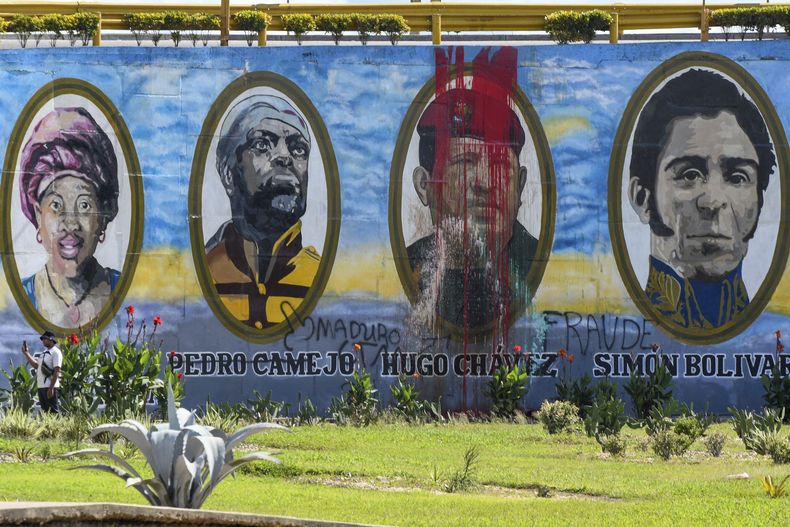 Un mural con pintura roja mancha el rostro del fallecido presidente venezolano Hugo Chávez, en el que aparece junto a héroes nacionales históricos, tras las protestas en contra de los resultados oficiales de las elecciones que declararon ganador al protegido de Chávez, el presidente Nicolás Maduro, en Valencia, Venezuela, el martes 30 de julio de 2024, dos días después de las elecciones. (AP Foto/Jacinto Oliveros)