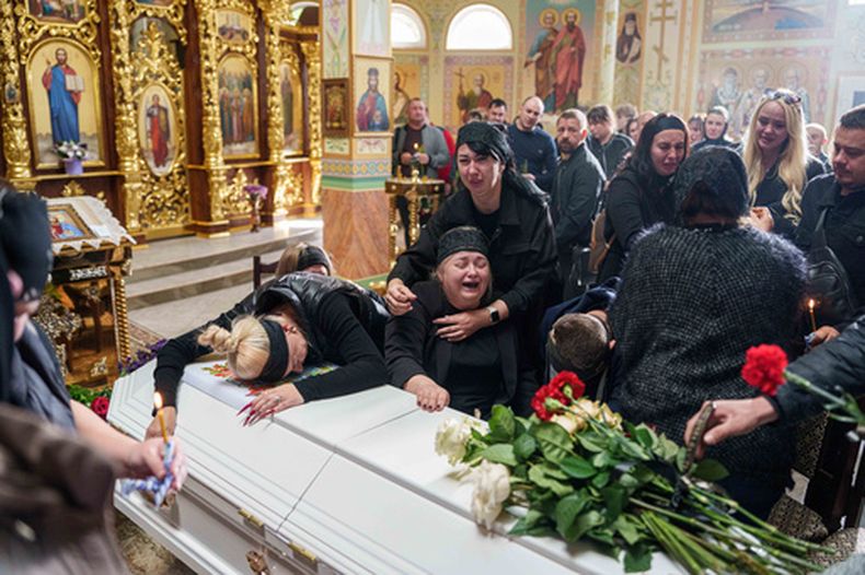 Una madre rodeada por familiares llora sentada junto al ataúd de su hijo Illia Honcharenko, de 14 años, asesinado por un ataque ruso con cohete contra una vivienda el 30 de septiembre, durante su funeral en Vyshhorod, en la región de Kiev, Ucrania el viernes 2 de octubre de 2026. (AP Foto/Evgeniy Maloletka)