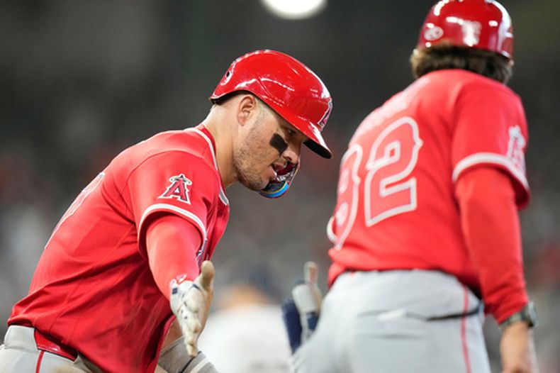 Mike Trout, de los Angelinos de Los Ángeles, extiende el brazo para intercambiar una palmada con el coach de la inicial Adam Eaton, tras conseguir un jonrón ante los Astros de Houston, el jueves 26 de marzo de 2026 (AP Foto/David J. Phillip)