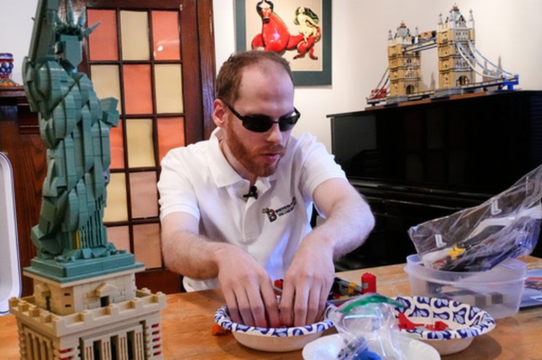 Matthew Shifrin, fundador de Bricks for the Blind, palpa piezas específicas mientras construye una máquina expendedora de chicles a base de piezas de Lego en la casa de su familia, el viernes 20 de marzo de 2026, en Newton, Massachusetts. (AP Foto/Charles Krupa)