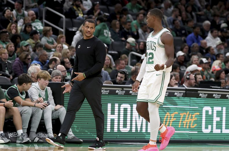 El entrenador en jefe de los Celtics de Boston, Joe Mazzulla, al frente a la izquierda, habla con el escolta de los Celtics, Lonnie Walker IV (12), quien camina hacia el banquillo del equipo durante la segunda mitad de un partido de baloncesto de la NBA de pretemporada contra los Raptors de Toronto, el domingo 13 de octubre de 2024, en Boston. (AP Foto/Mark Stockwell)