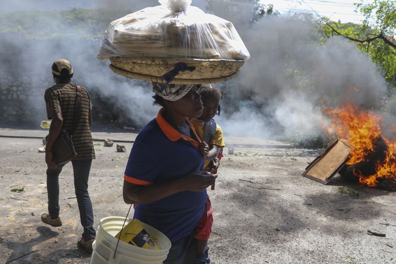Una vendedora callejera y su hija caminan frente a una barricada en llamas colocada por manifestantes durante una protesta contra la inseguridad en Puerto Príncipe, Haití, el miércoles 19 de marzo de 2025. (AP Foto/Odelyn Joseph)