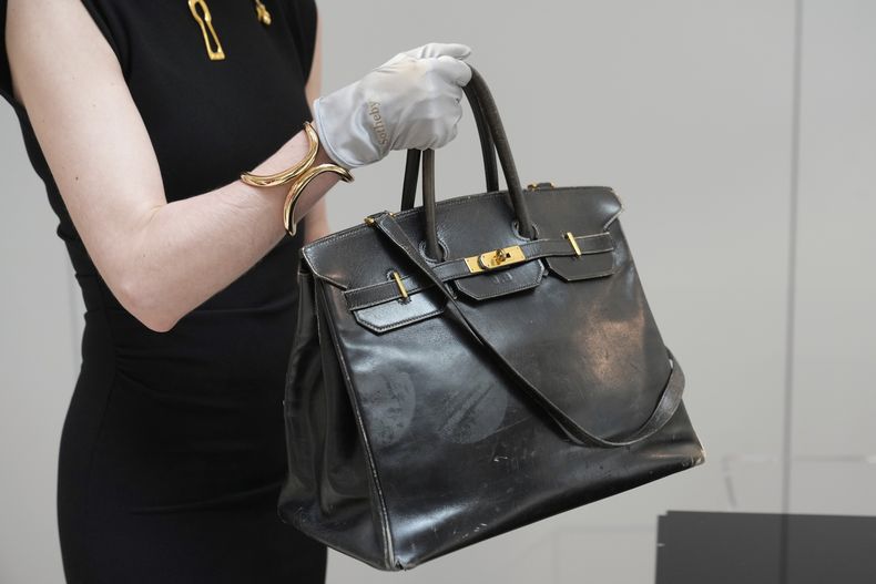 Un oficial de subasta carga el bolso Birkin original creado por Hermès para Jane Birkin en 1984, antes de su subasta el jueves 10 de julio de 2025 en París. (Foto AP/Michel Euler)