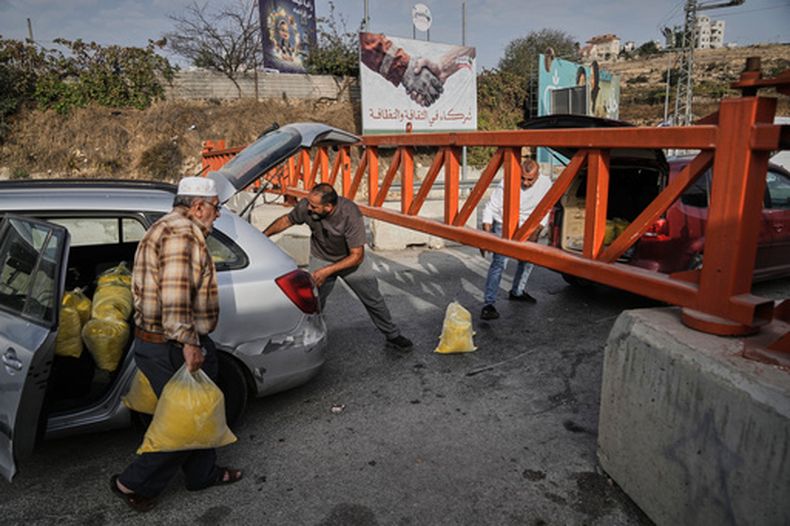 Palestinos cargan bolsas de harina de semolina a través de una puerta militar cerrada a vehículos durante una operación militar israelí en Hebrón, en la ocupada Cisjordania, el sábado 24 de octubre de 2026, al día siguiente de un ataque palestino en la zona. (AP Foto/Mahmoud Illean)