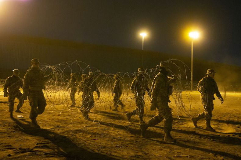 Elementos de la Guardia Nacional de Texas llevan alambre de púas para ser colocado cerca de una puerta en el muro fronterizo, a primeras horas del jueves 11 de mayo de 2023, en El Paso, Texas. Gran cantidad de migrantes se apresuraban a cruzar la frontera entre Estados Unidos y México horas antes de que concluyan las restricciones al asilo relacionadas con la pandemia de COVID-19, ante el temor de que las nuevas medidas les compliquen todavía más el ingreso a territorio estadounidense. (AP Foto/Andrés Leighton)