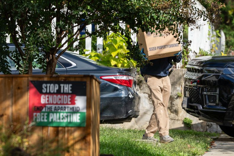 En esta imagen tomada el lunes 12 de octubre de 2026, se ven carteles en la propiedad de un vecino de la representante federal demócrata por Minnesota Ilhan Omar, mientras agentes del Departamento de Seguridad Nacional transportan cajas durante un registro en la residencia de Omar en Washington. (AP Foto/J. Scott Applewhite)