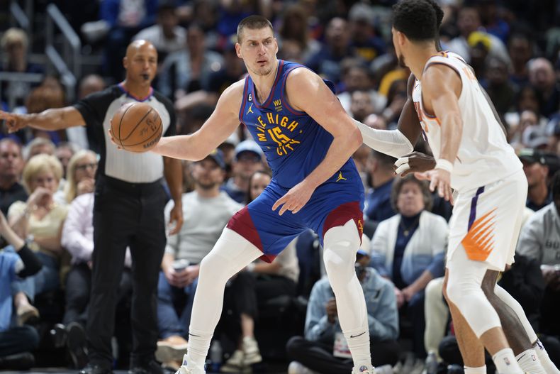 El serbio Nikola Jokic, de los Nuggets de Denver, busca enviar un pase frente a Devin Booker, de los Suns de Phoenix, en el encuentro de playoffs disputado el sábado 29 de abril de 2023 (AP Foto/David Zalubowski)