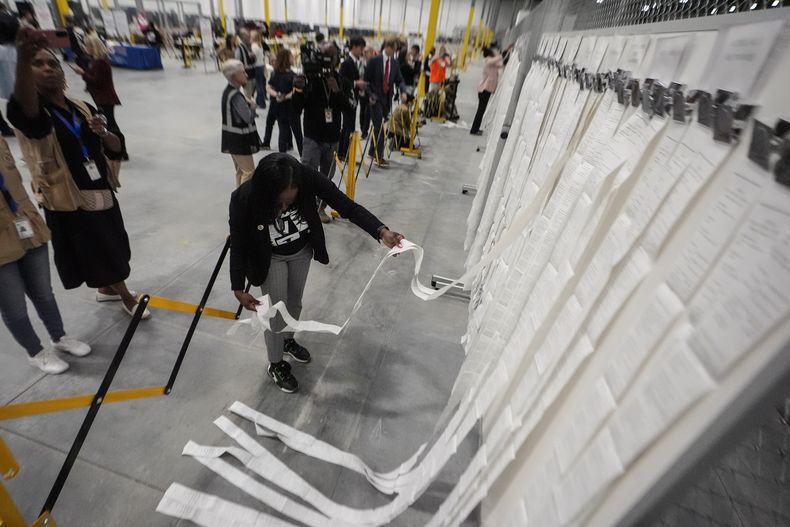 Una empleada electoral cuelgas las cintas de lectura utilizadas en el voto anticipado en el centro operativo y electoral del condado de Fulton, el 5 de noviembre de 2024, en Atlanta. (AP Foto/John Bazemore)