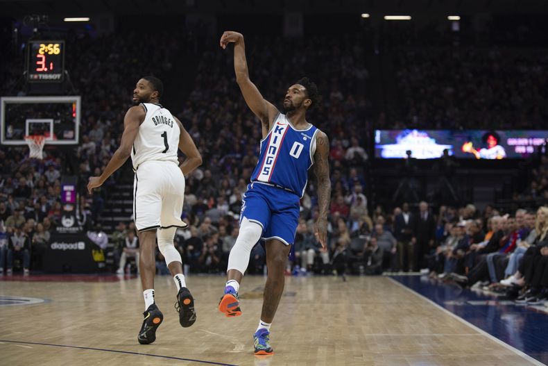 Malik Monk (0), de los Kings de Sacramento, hace un seguimiento después de tomar un tiro de larga distancia, mientras que Mikal Bridges (1), de los Nets de Brooklyn, observa durante el primer cuarto del juego de baloncesto de la NBA, el lunes 11 de diciembre de 2023, en Sacramento, California. (AP Foto/José Luis Villegas)