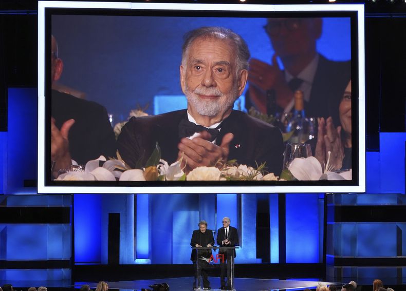 El cineasta Francis Ford Coppola aparece en la pantalla mientras los actores Al Pacino, a la izquierda, y Robert De Niro, hablan sobre su trayectoria durante un tributo a la trayectoria de Coppola en la 50ma entrega de los premios AFI, el sábado 26 de abril de 2025, en Los Ángeles. (AP Foto/Chris Pizzello)