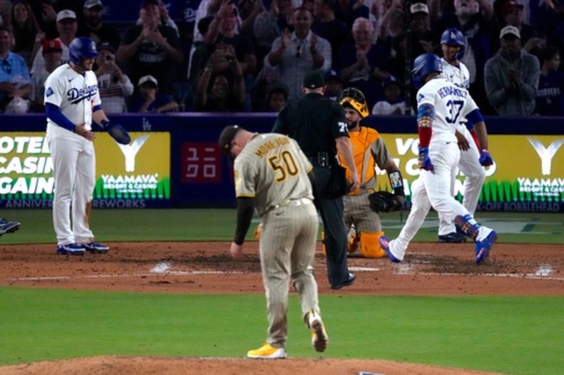 Teoscar Hernández (derecha), de los Dodgers de Los Ángeles, anota tras conectar un grand slam mientras Max Muncy (izquierda) lo espera y el lanzador de los Padres de San Diego, Adrián Morejón, permanece en el montículo durante la séptima entrada de un partido de béisbol, el viernes 3 de julio de 2026, en Los Ángeles. (Foto AP/Mark J. Terrill)