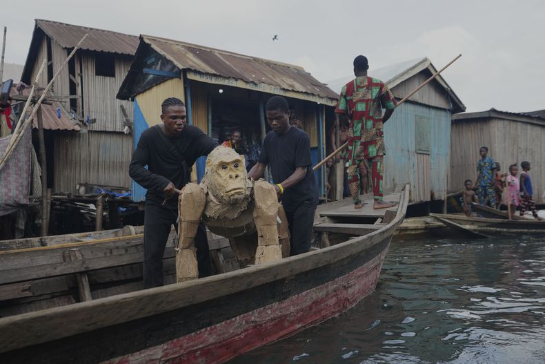 Titiriteros transportan animales de cartón en canoas en el barrio pobre de Makoko en Lagos, Nigeria, el sábado 19 de abril de 2025, parte de The Herds, un teatro itinerante que se desplaza desde la República Democrática del Congo hasta el Círculo Ártico en un intento por atraer la atención hacia la crisis climática. (AP Foto/Sunday Alamba)