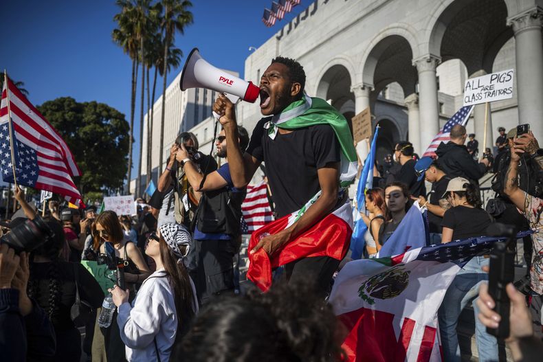 Un hombre grita a través de un megáfono fuera del Ayuntamiento de la ciudad durante las protestas por las redadas de inmigración, el miércoles 11 de junio de 2025, en Los Ángeles. (AP Foto/Ethan Swope)