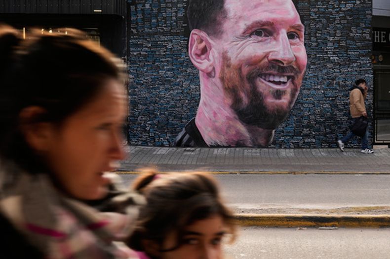 La gente pasa junto a un mural de Lionel Messi, obra del artista Leonel García, en el que figuran los nombres de admiradores escritos por ellos mismos como homenaje al futbolista, en Berazategui, a las afueras de Buenos Aires (Argentina), el lunes 22 de junio de 2026. (Foto AP/Gustavo Garello)