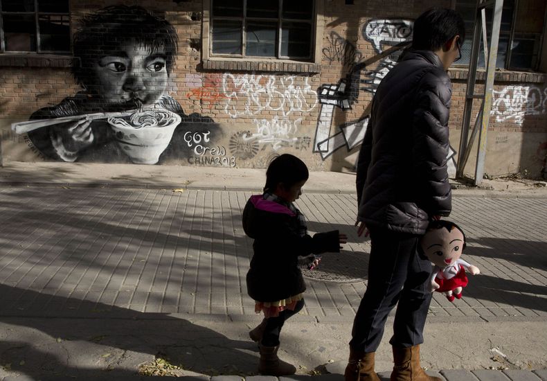 Una mujer camina con una ni&ntilde;a el 17 de noviembre de 2013 cerca de un mural que describe a un ni&ntilde;o comiendo en Beijing. China autoriz&oacute; formalmente el s&aacute;bado 28 de diciembre de 2013 que las parejas tengan un segundo hijo si algun