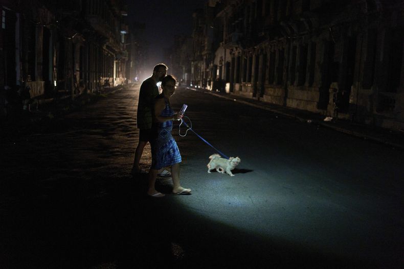 La gente enciende una linterna mientras cruza una calle con su perro durante un apagón en La Habana, el miércoles 10 de septiembre de 2025. (AP Foto/Ramón Espinosa)