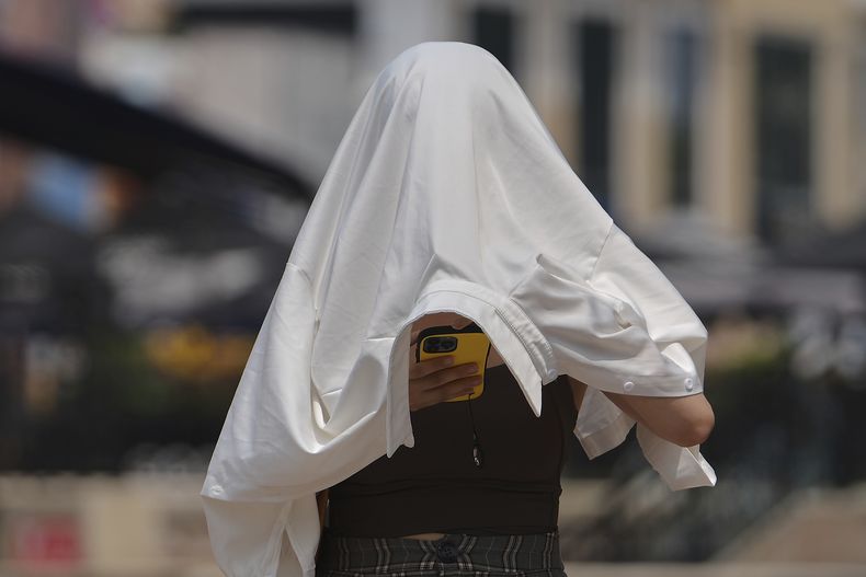 ARCHIVO – Una mujer se protege del sol mientras revisa su teléfono en un día caluroso en una calle de Beijing, el miércoles 23 de julio de 2025. (AP Foto/Andy Wong, Archivo)