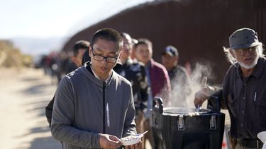 Un chino recibe avena cocida de manos de un voluntario mientras aguarda junto con otras personas a solicitar asilo tras cruzar la frontera con México, el martes 24 de octubre de 2023, cerca de Jacumba, California. (AP Foto/Gregory Bull)