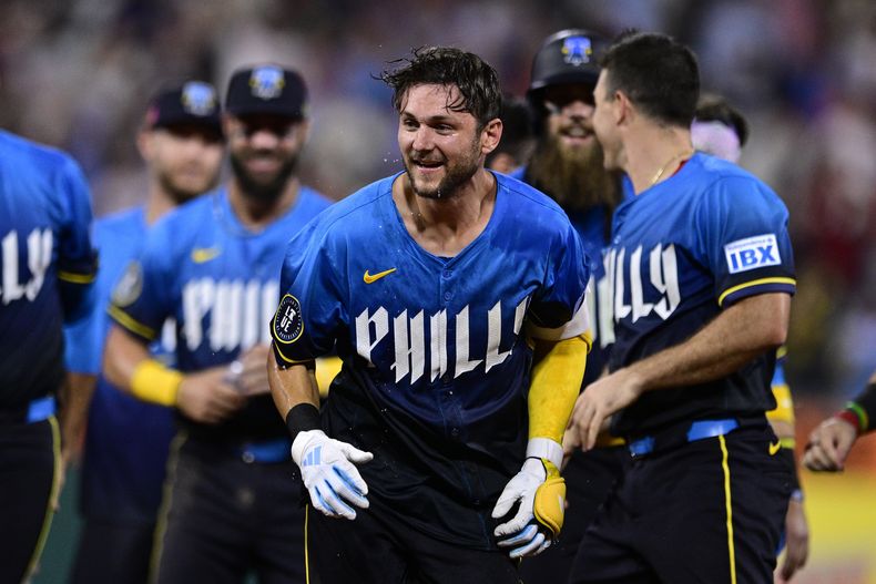 Trea Turner (centro) celebra junto a sus compañeros de equipo luego de conectar un sencillo decisivo ante el lanzador de los Nacionales, Kyle Finnegan durante la novena entrada del juego de béisbol, el viernes 16 de agosto de 2024, en Filadelfia. (AP Foto/Derik Hamilton)