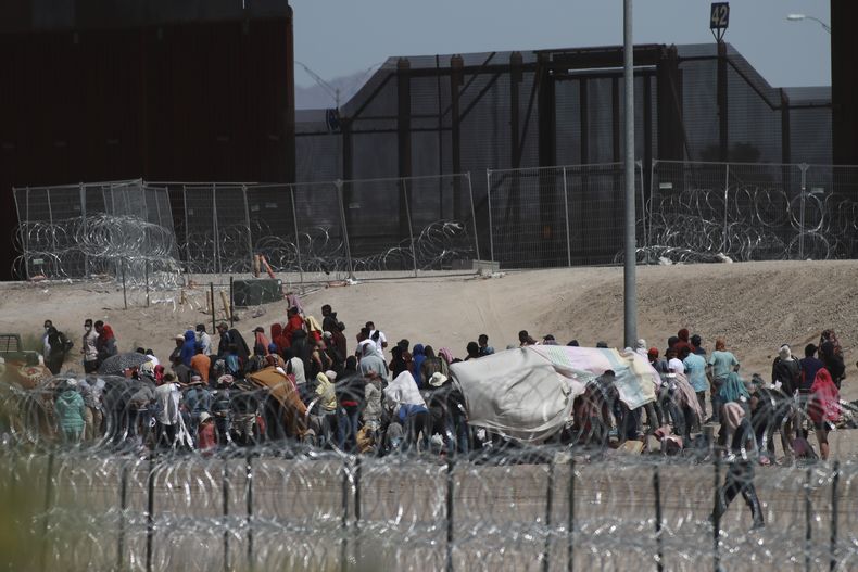Un grupo de migrantes aguarda la llegada de las autoridades estadounidenses entre una barricada de alambre de púas y un muro fronterizo el miércoles 10 de mayo de 2023, en esta fotografía tomada desde Ciudad Juárez, México. A partir del 11 de mayo, Estados Unidos comenzará a negarle el asilo a los migrantes que se presenten en la frontera con México sin que primero hayan presentado una solicitud en línea o pedido protección en el país por el que pasaron, según una nueva regla aprobada el 10 de mayo. (AP Foto/Christian Chávez)