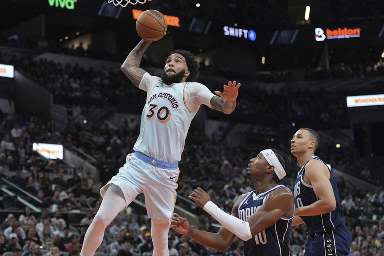 El alero de los Spurs de San Antonio Julian Champagnie avanza hacia la canasta frente al base de los Mavericks de Dallas Brandon Williams en el encuentro del miércoles 12 de marzo del 2025. (AP Foto/Eric Gay)