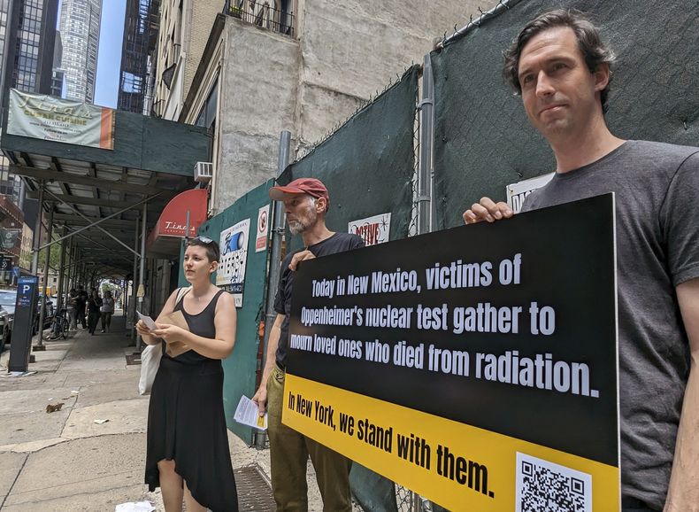 Matthew Bolton, a la derecha, y Jan-Christoph Zoels, al centro, sostienen un cartel mientras se manifiestan en la ciudad de Nueva York el 15 de julio de 2023. Activistas se reunieron para llamar la atención hacia los residentes de Nuevo México que estuvieron expuestos a la radiación durante la prueba atómica Trinity realizada en 1945 como parte del Proyecto Manhattan. El mitin procedió a una proyección y un panel de discusión sobre la nueva película Oppenheimer. (Andrew Facini vía AP)