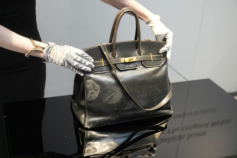 Un oficial de subasta muestra el bolso Birkin original creado por Hermès para Jane Birkin en 1984, antes de su subasta el jueves 10 de julio de 2025 en París. (AP Photo/Michel Euler)