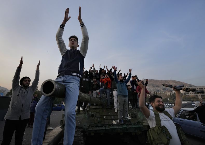 Ciudadanos sirios sobre un tanque de las fuerza gubernamentales que fue abandonado sobre una calle, mientras celebraban durante el segundo día de la toma de la ciudad a manos de los insurgentes, el lunes 9 de diciembre de 2024, en Damasco, Siria. (AP Foto/Hussein Malla)