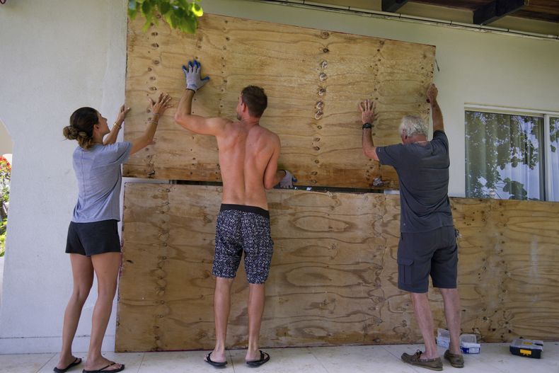 Tres personas cubren las ventanas de su hogar en preparación para la llegada del huracán Beryl el domingo 30 de junio de 2024, en Bridgetown, Barbados. (AP Foto/Ramón Espinosa)