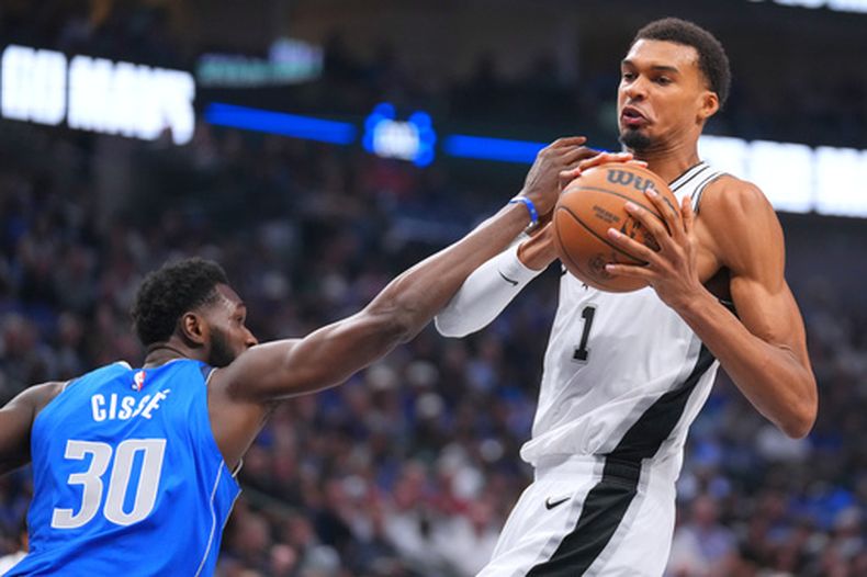 El delantero de los Spurs de San Antonio, Victor Wembanyama, a la derecha, intenta controlar el balón tras un rebote mientras el pívot de los Mavericks de Dallas, Moussa Cisse, trata de incomodarlo durante la primera mitad de un partido de básquetbol de la NBA, el sábado 24 de octubre de 2026, en Dallas. (Foto AP/Julio Cortez)