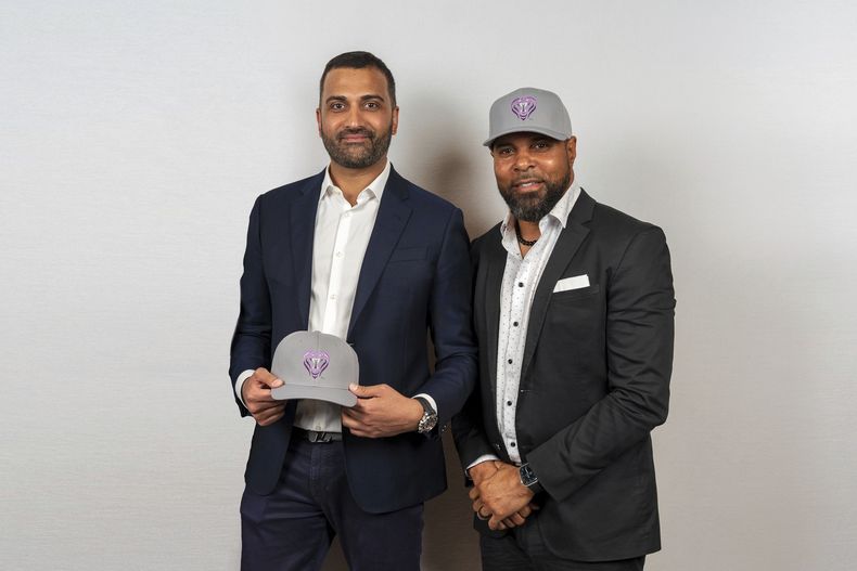 En esta foto suministrada por Baseball United, el ex Grandes Ligas Barry Larkin (derecha), codueño de Baseball United, y Kash Shaik, CEO y codueño de Baseball United, posan con los gorros de Mumbai Cobras en la presentación de la franquicia en Cincinnati, Ohio, el viernes 5 de mayo de 2023. (Baseball United, Inc. vía AP)