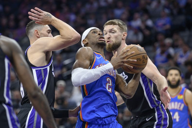 Shai Gilgeous-Alexander, del Thunder de Oklahoma City, elude a Zach LaVine (izquierda) y a Domantas Sabonis, de los Kings de Sacramento, en el partido del martes 25 de marzo de 2025 (AP Foto/Randall Benton)