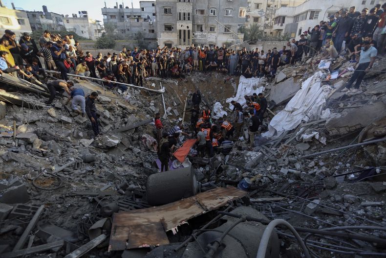 Palestinos reunidos en torno a los restos de una casa destruida tras ataques israelíes en Ciudad de Gaza, Franja de Gaza, el sábado 21 de octubre de 2023. (AP Foto/Abed Khaled)