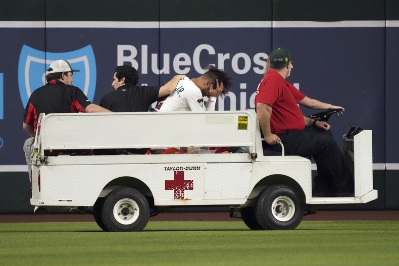 El cubano Lourdes Gurriel Jr., tercero por la izquierda, de los Diamondbacks de Arizona, es retirado en un carrito después de lanzarse a por una pelota bateada por Rowdy Tellez, de los Rangers de Texas, en la sexta entrada de un juego de béisbol, el lunes 1 de septiembre de 2025, en Phoenix. (AP Photo/Rick Scuteri)