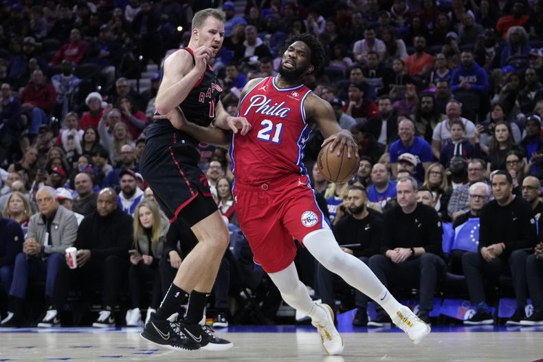 Joel Embiid de los 76ers de Filadelfia (derecha) intenta superar a Jakob Poeltl de los Raptors de Toronto durante la primera mitad del juego de la NBA, el viernes 22 de diciembre de 2023, en Filadelfia. AP Foto/Matt Slocum)