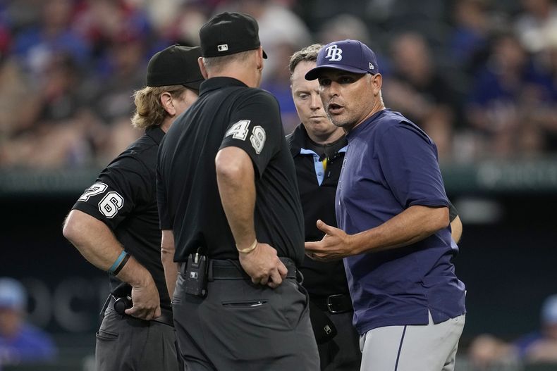 El mánager de los Rays de Tampa Bay, Kevin Cash (derecha) conversa con los árbitros Andy Fletcher (49) y Mike Muchlinski (76) luego que el mexicano Randy Arozarena fue decretado out en su turno al bate debido a una interferencia de un fanático en el séptimo episodio del juego de béisbol ante los Rangers de Texas, en Arlington, Texas, el domingo 7 de julio de 2024. (AP Foto/Tony Gutierrez)