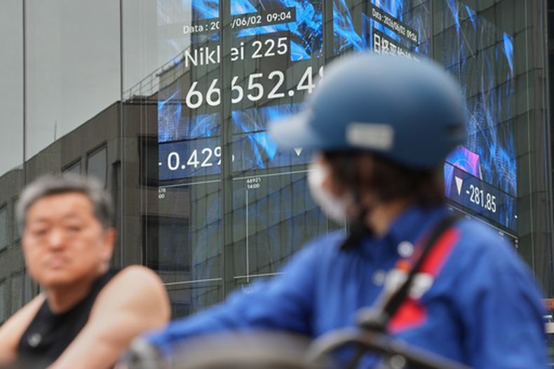 Varias personas pasan frente a una pantalla electrónica que muestra el índice Nikkei de Japón en una correduría de valores el martes 2 de junio de 2026, en Tokio. (AP Foto/Eugene Hoshiko)
