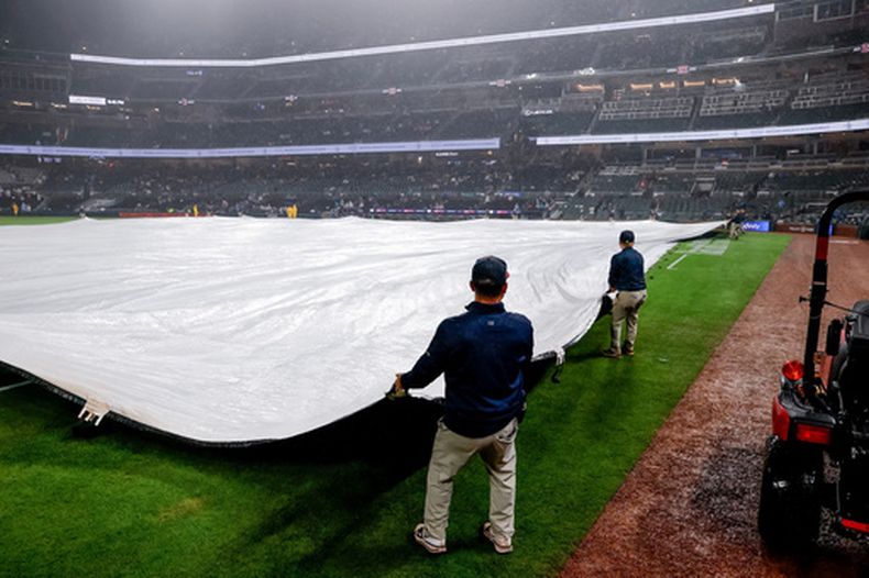El personal del campo de los Bravos de Atlanta cubre el cuadro con una lona luego de que el juego fuera suspendido debido al clima en la segunda entrada de un partido de béisbol, el martes 16 de junio de 2026, en Atlanta. (Foto AP/Erik S. Lesser)