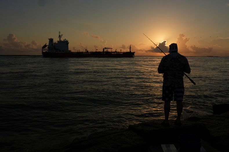 ARCHIVO - Un petrolero navega al amanecer mientras un hombre pesca en la orilla en Port Aransas, Texas, el 9 de agosto de 2025. (AP Foto/Eric Gay, ARCHIVO)