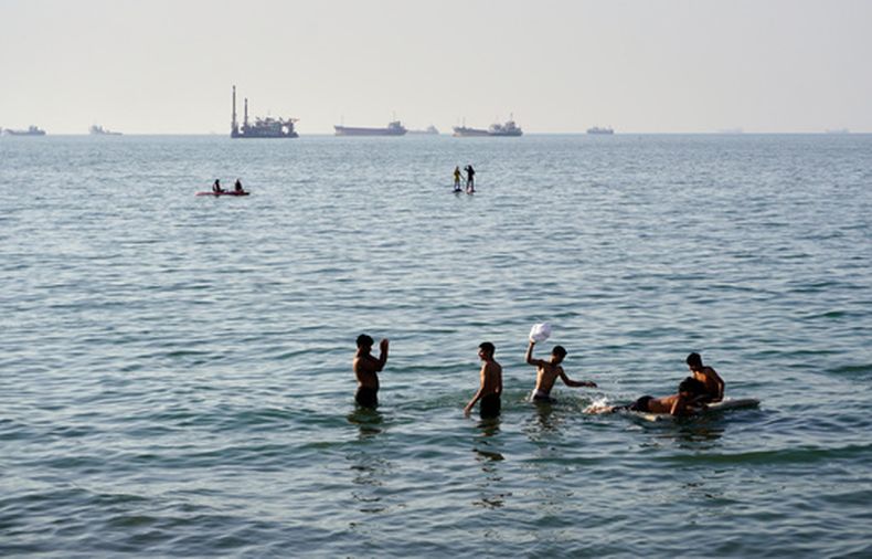 Personas nadan y juegan en las aguas del estrecho de Ormuz al tiempo que buques de carga y embarcaciones comerciales permanecen anclados a lo lejos, frente a Bandar Abbas, Irán, el miércoles 10 de junio de 2026. (Razieh Poudat/ISNA vía AP)