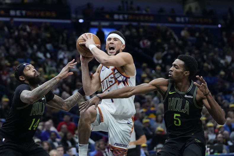 El escolta de los Suns de Phoenix Devin Booker (1) va a la canasta entre el alero de los Pelicans de Nueva Orleans Brandon Ingram (14) y el alero Herbert Jones (5) en la segunda mitad del partido de baloncesto de la NBA en Nueva Orleans, el viernes 19 de enero de 2024. Los Suns ganaron 123-109. (AP Foto/Gerald Herbert)