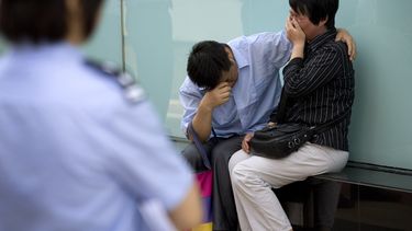 americateve | Una polic&iacute;a observa a una pareja llorar porque representantes de la aerol&iacute;nea Malaysia Airlines se negaron a recibirlos en las oficinas de la empresa en Beijing, China, el mi&eacute;rcoles 11 de junio de 2014. El hijo de la pareja era una de